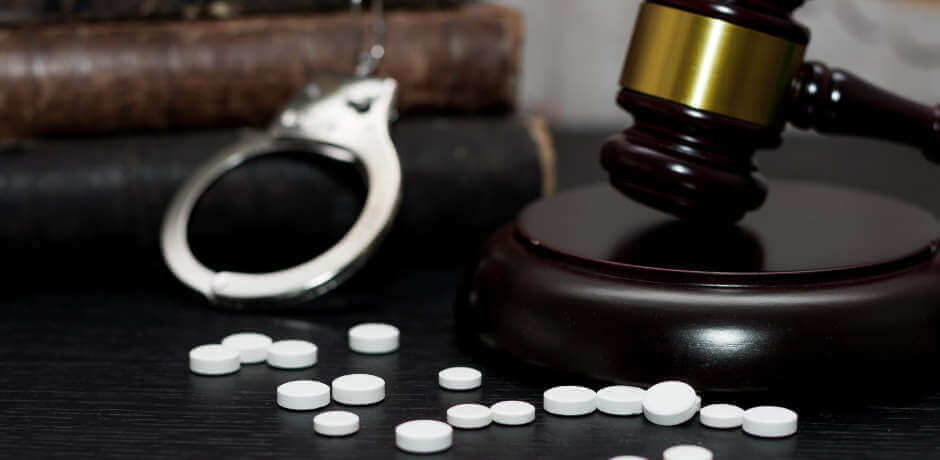 pills and judge's gavel with handcuffs and books in the background